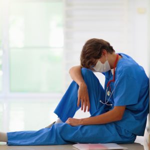 A nurse wearing a mask and scrubs looking upset